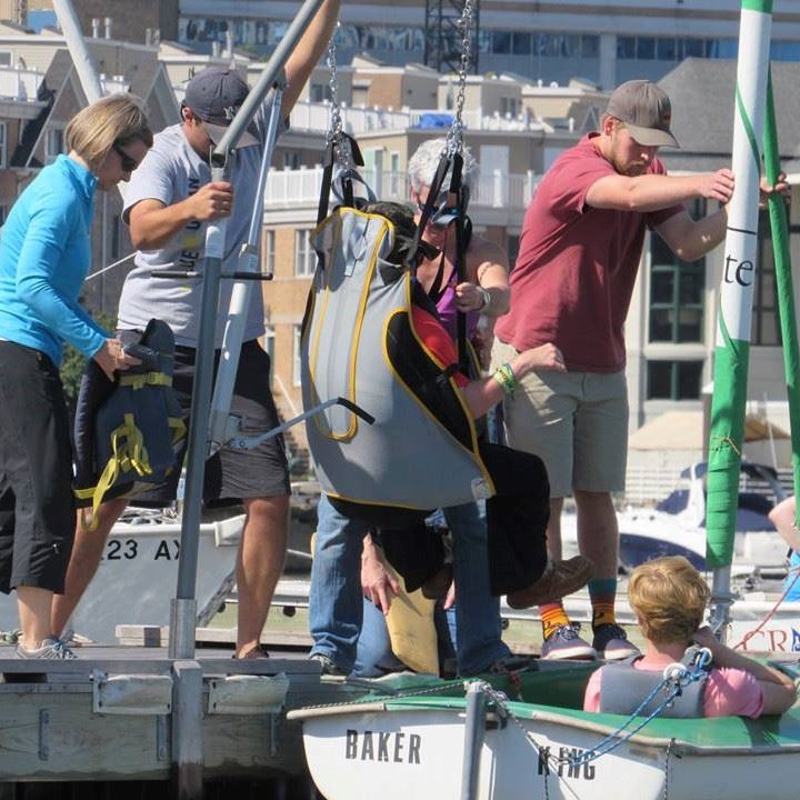 Volunteers assist with a hoyer lift transfer into a Hansa/Access dinghy