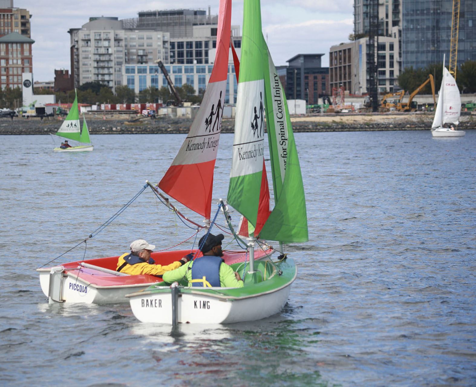 Two Adaptive sailors sailing colorful dinghies in Baltimore harbor