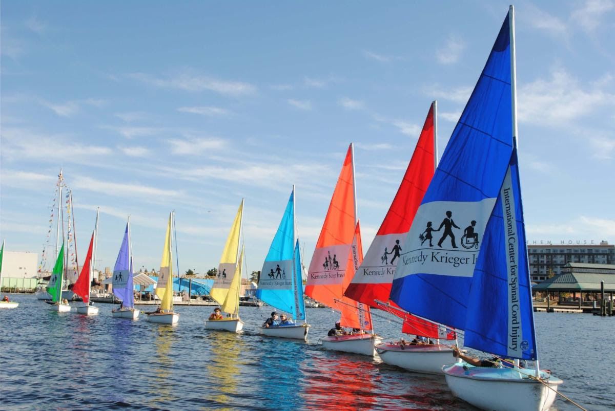 Nine colorful Hansa 303 dinghies being towed in a line away from the dock 